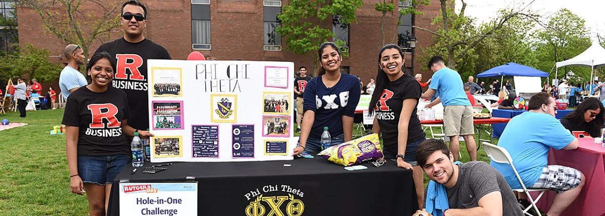 Phi Chi Theta and a pet dog pose at their Hole-in-One challenge table