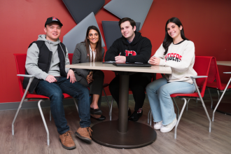 four students sitting at a table smiling for the camera